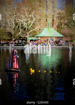 Remote controlled sailboat toys and whimsical rubber ducky parade at the Conservatory water on a spring afternoon day, Central Park, New York City, USA Stock Photo