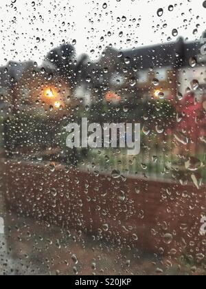 Looking out of a window covered with raindrops, residential area with lights in the early evening Stock Photo
