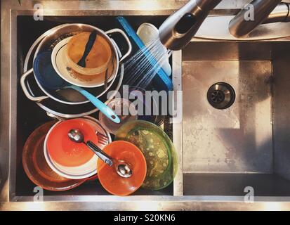 From above flat lay view of rinsing dirty dishes with sprayer faucet in a large rectangular stainless steel sink Stock Photo