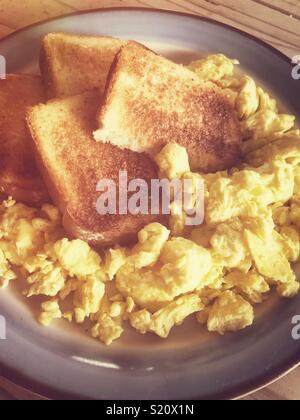 Scrambled eggs and toast on a plate in warm morning light Stock Photo