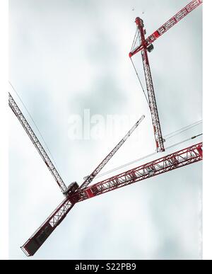 Three red cranes against a grey sky Stock Photo