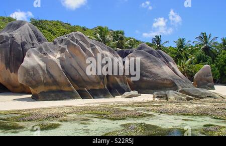 Typical rock formation with traces of erosion on the beach in the Seychelles. Three boulders on the white sand beach in front of the green countryside and blue sky Stock Photo