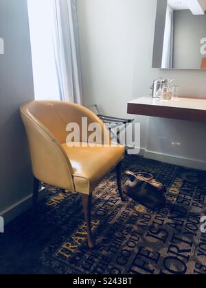 Hotel room with yellow armchair and brown women’s handbag on the floor Stock Photo
