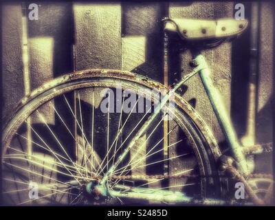 Rusty old bicycle parked against a wooden fence Stock Photo