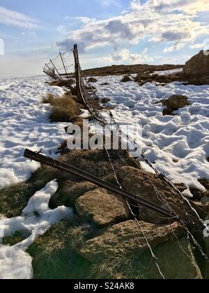 A broken barbed wire fence on a snow-covered plateau in the Drakensberg Mountains marks the border between South Africa and Lesotho. Stock Photo