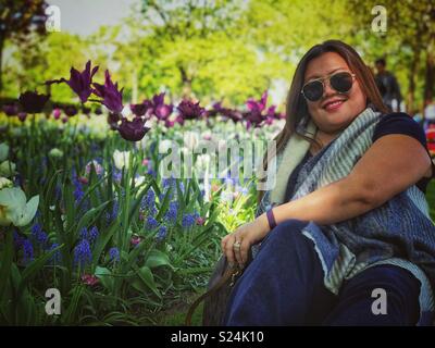 A lady poses for a photo sat in a garden. Stock Photo