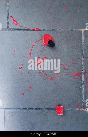 Broken red nail varnish bottle on a tiled floor Stock Photo