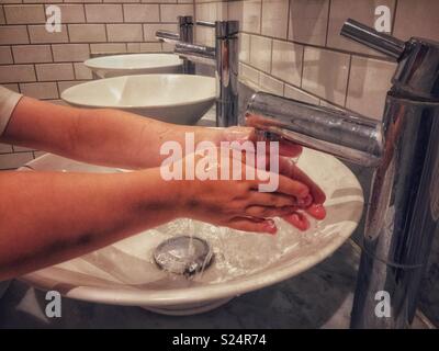 A young boy washes his hands at a sink in a public toilet. Stock Photo