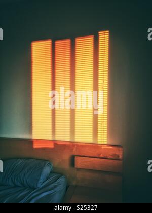 Brilliant orange patterns on bedroom wall from sunrise shining through window blinds. Stock Photo