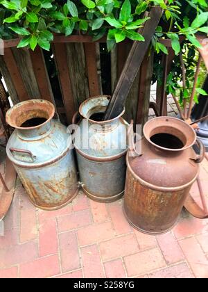 Three old milk cans by a wooden fence Stock Photo