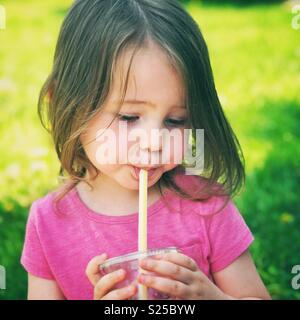 Toddler girl drinking juice from a plastic cup with a straw outside at a picnic Stock Photo