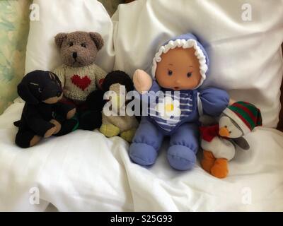 Stuffed animals and a baby doll sit comfortably on a big white pillow. Stock Photo