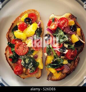 Two slices of oven toasted homemade bread with chopped roasted vegetables lightly sprinkled with Parmesan cheese on a white plate Stock Photo