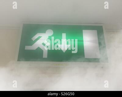 Green illuminated fire escape sign above doorway, about to be engulfed by smoke. Where there's smoke there's fire Stock Photo