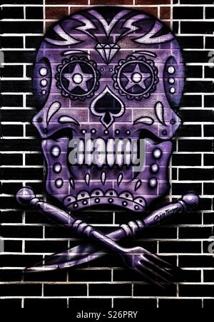 Skull and crossed-cutlery artwork on a restaurant wall at Cancun airport, Mexico. Artwork signed by Craig Fraser. Stock Photo
