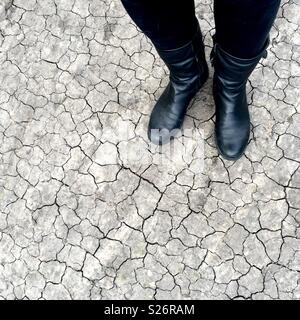 Person wearing black jeans and black boots standing on dry cracked earth Stock Photo