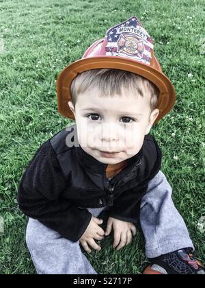 Little boy sitting in grass wearing fireman helmet, with grungify filter Stock Photo