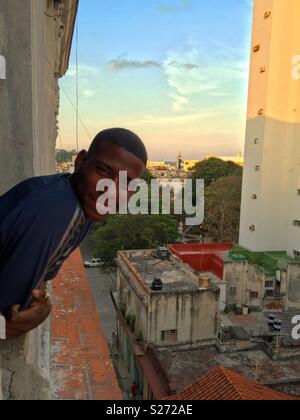 Local Cuban boy in old Havana looking out of his apartment complex at sunset Stock Photo