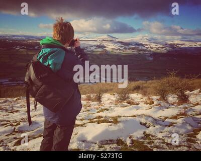 A young boy takes a photo from the Skirrid mountain, of the Snow covered Sugarloaf Mountain near Abergavenny, Brecon Beacons, Wales, U.K. Stock Photo