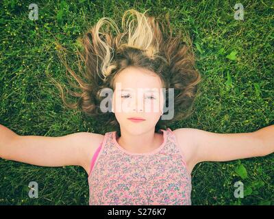 11 year old girl laying in the grass with arms out and serious expression on her face Stock Photo