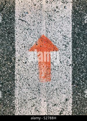 An orange arrow painted on a road. Stock Photo