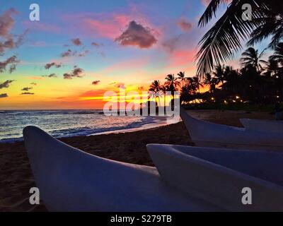 Outrigger canoes beached for the day as the sun sets over the beautiful tropical Pacific Ocean in Hawaii Stock Photo