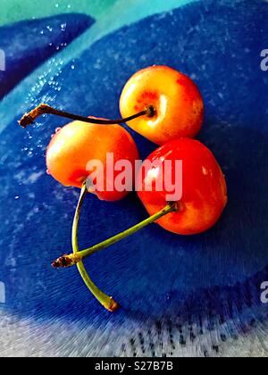 Three fresh cherries on a blue glass surface Stock Photo