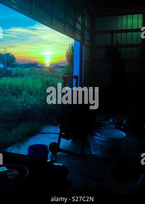 Blue tinted photo of sunset outside garage door opening in shed containing honey extraction equipment Stock Photo