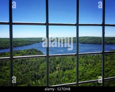 Looking down to sapphire blue lake and emerald green forest through bars from Dorset fire tower in Northern Ontario. Stock Photo