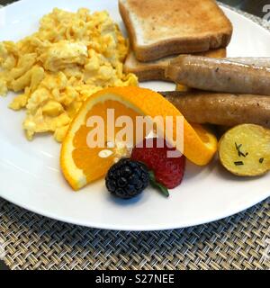 A beautifully plated breakfast of scrambled eggs, toast, potatoes, sausage and fruit garnish Stock Photo