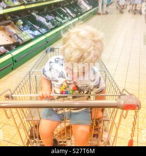 Two year old baby boy falling asleep in a supermarket shopping trolley,Hampshire, England, United Kingdom. Stock Photo