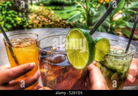 Happy Hour, cocktails, Mojito, rum and coke, poncha, all with ice and a slice of lime, in women’s hands, at a table outdoors in Funchal, Madeira, Portugal Stock Photo