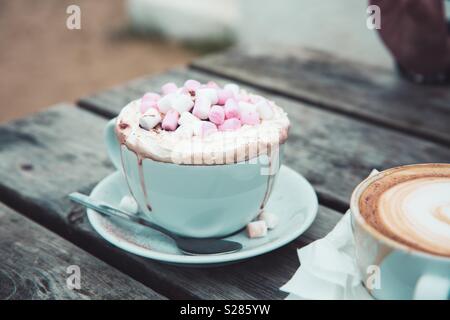 A luxurious hot chocolate drink in a cup and saucer with whipped cream and marshmallows outdoors Stock Photo