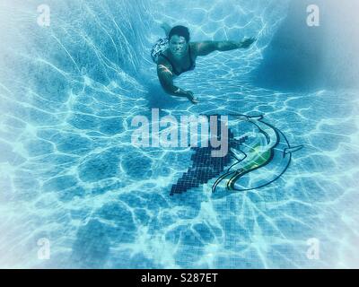 Millennial swimming underwater, in a tiled swimming pool with a dolphin mosaic. Stock Photo