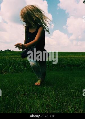 Young blonde haired girl running in a green field with blue sky Stock Photo