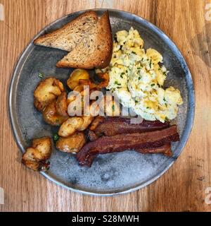 An overhead view of a breakfast of scrambled eggs, bacon, potatoes and toast on a rustic metal plate Stock Photo