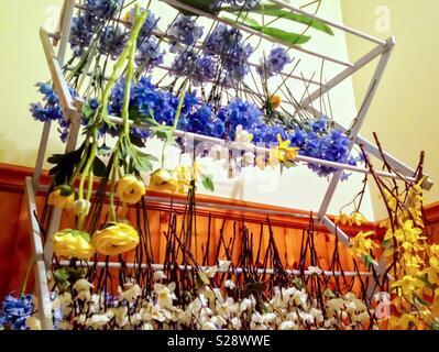 Blue, yellow, and white silk flowers- freshly washed in soapy water- hung to dry on wooden rack Stock Photo