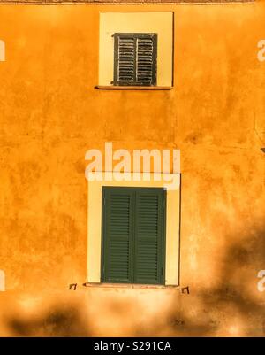 Small and large green shuttered windows in yellow plaster wall Stock Photo