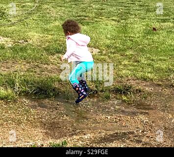 Little girl jumping in rain puddle. Caught in mid air. Loves her rain boots. Stock Photo