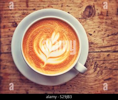 An overhead view of a cup of Latte coffee. An interesting outline shape of white milk predominates. You can’t beat a rustic wooden table for a background! Photo Credit - © COLIN HOSKINS. Stock Photo