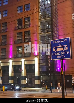 Manchester City centre at night  looking colourful with vibrant lighting. Pedestrians are warned to look both ways for oncoming trams when crossing the road. Stock Photo