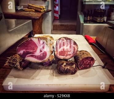 Dried, cured sausages on a chopping board inside a traditional Mediterranean delicatessen selling dried hams, sausages and cheeses. Stock Photo