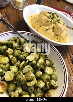 Roasted Brussel sprouts and whole steamed cheesy cauliflower in white dishes on a wooden table. Stock Photo