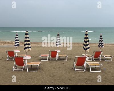 Rainy september day view over closed umbrellas and chaises longues on the beach Stock Photo