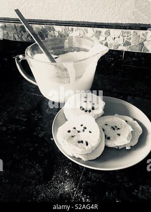 Baking pancakes in the morning for the family on the weekend. Plate of pancakes and bowl of pancake batter with wooden rubber stirring spoon Stock Photo