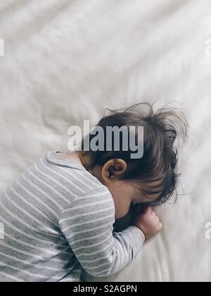 A young baby girl curled up asleep in her crib. Stock Photo