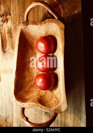 3 red ripe tomatoes in a wooden bowl with handles. Stock Photo