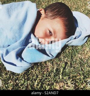 Five year old boy snuggles into his blue towel under the sun after a dip in the pool. Summer time, Portugal. Stock Photo