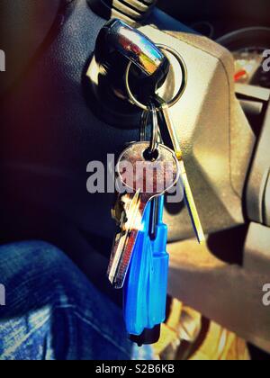 A bunch of keys dangle from a car key which is plugged into the car ignition. Stock Photo