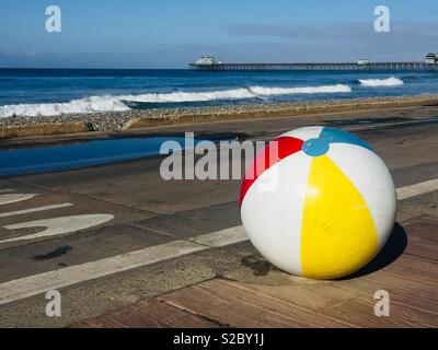A scenic view of the Oceanside, California pier from the public park by the beach. A cute, colorful cement barrier painted as a beach ball is in the foreground. Stock Photo